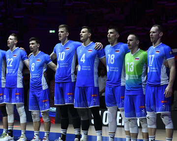 Slovenski odbojkarji v modrih reprezentančnih dresih in libero v zelenem dresu med postavitvijo ekipe pred začetkom tekme